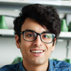 A friendly individual with short dark hair and specs grins at the camera, green storage bins lined up neatly on shelves behind them. - Barndominium Kansas